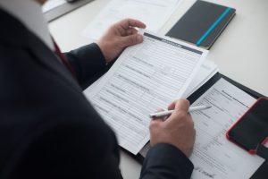 A businessman in a black suit reviews a printed application form with a pen on his desk.